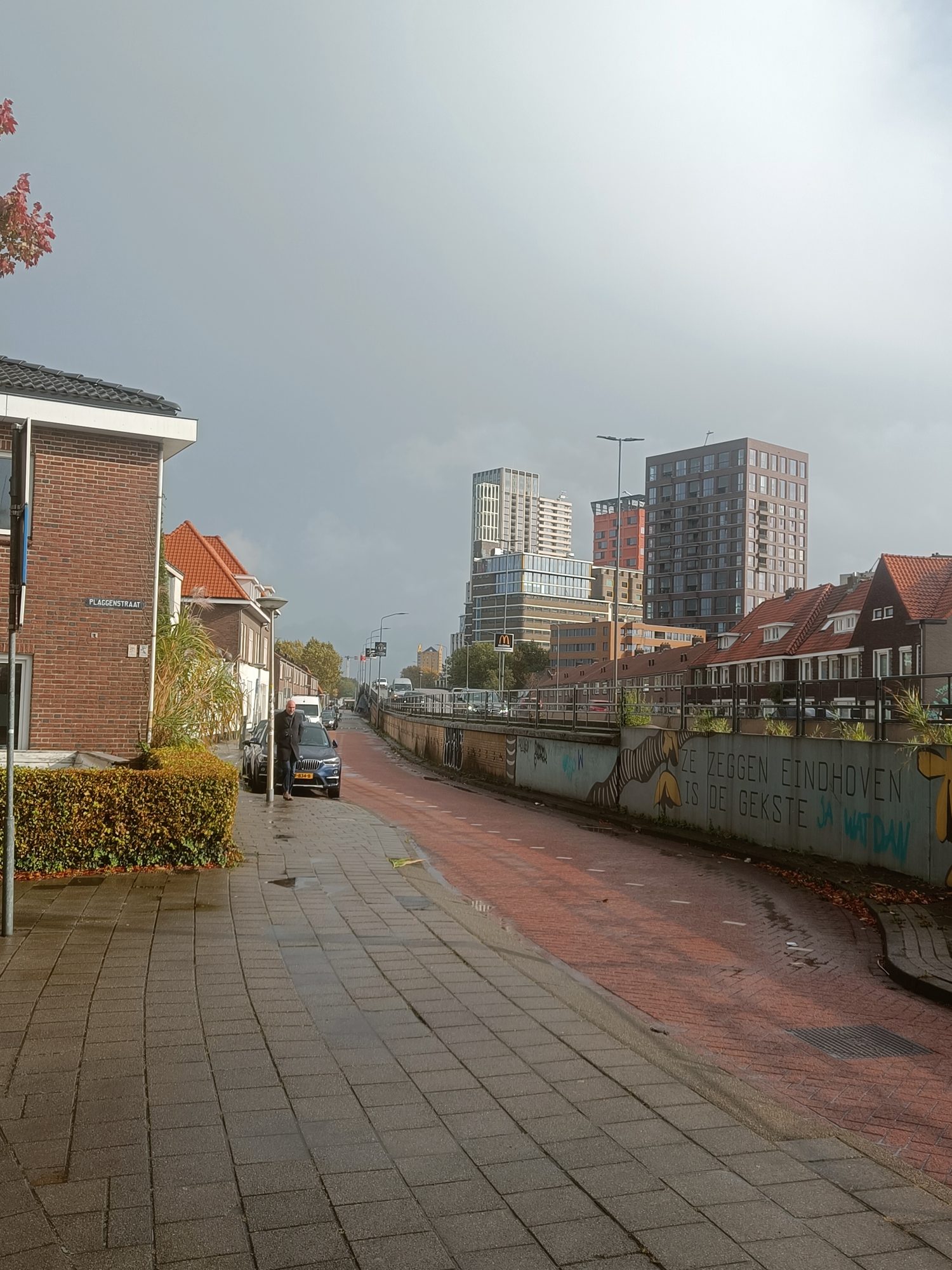 A quiet street of low brick houses with new towers rising behind