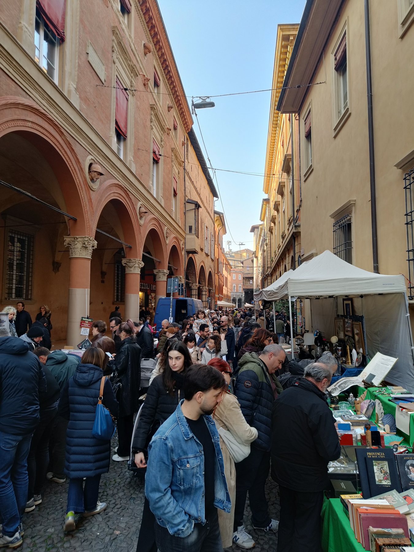 A crowd browsing book stalls under a white canopy in a portico street
