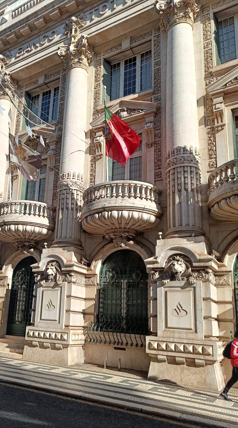 An ornate bank front with stone columns, balconies and the Portuguese flag