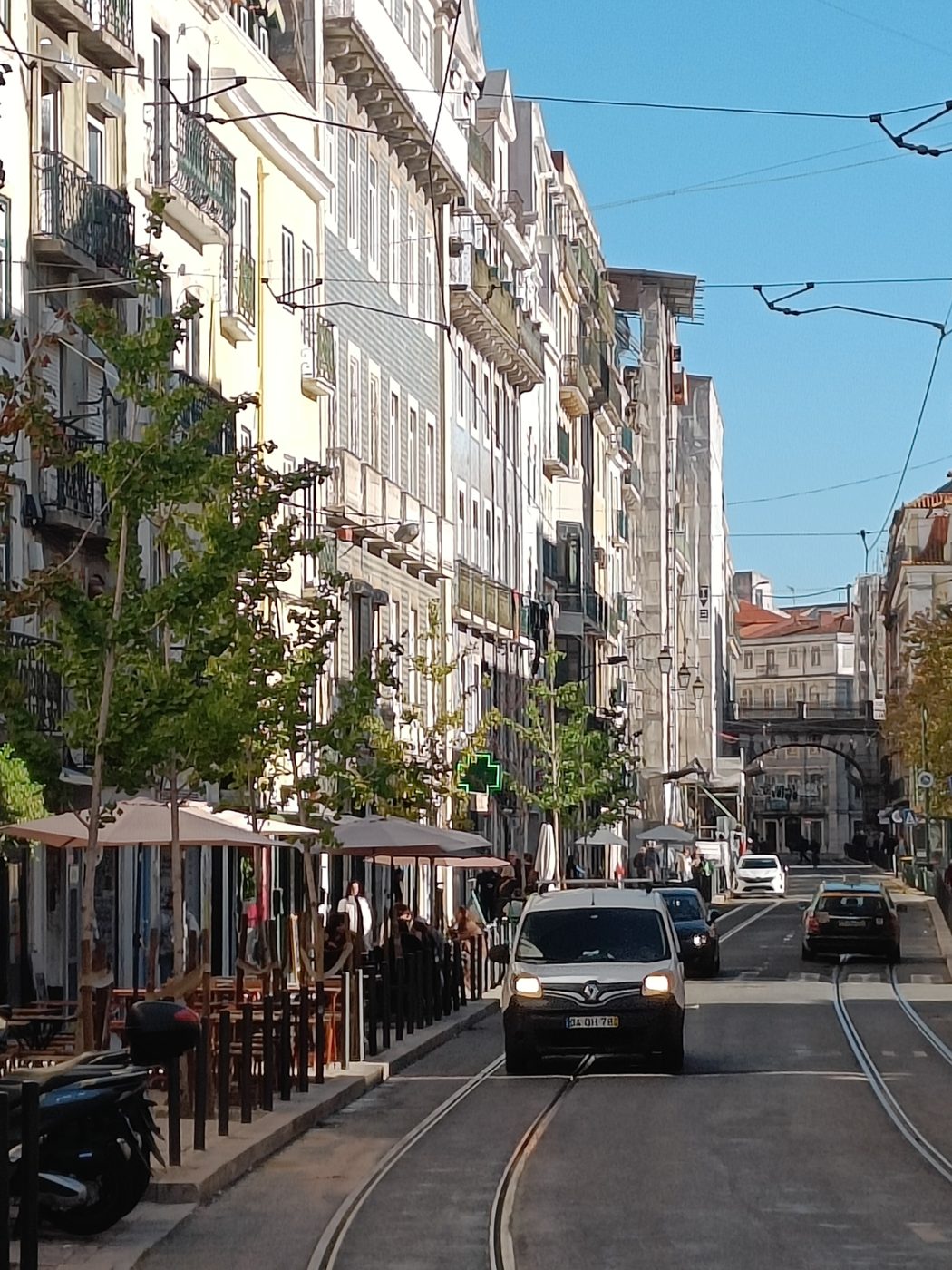 A street with tram tracks, café terraces under umbrellas and a van driving towards the camera