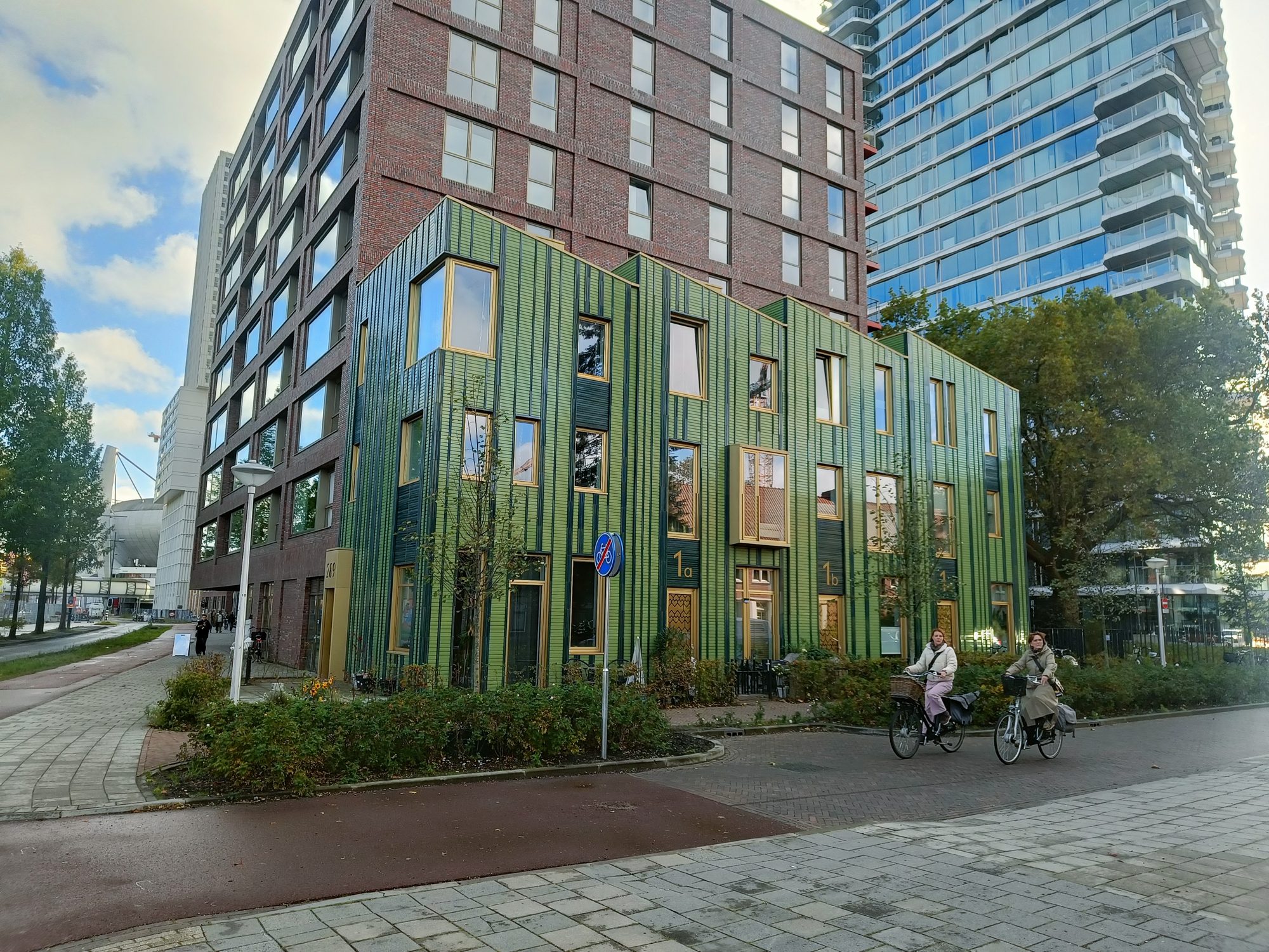 A new building clad in green panels, with two cyclists passing in front