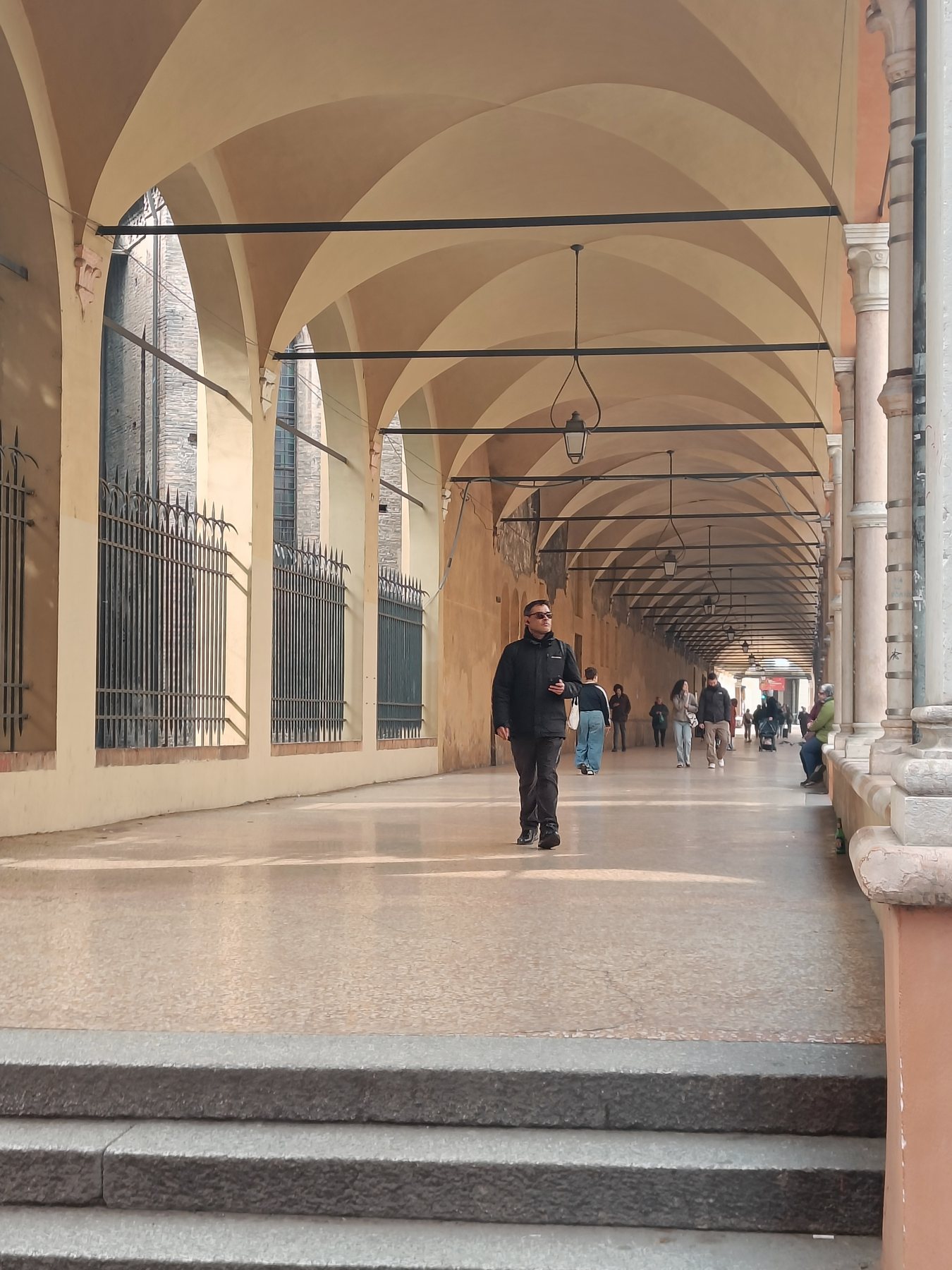 A long empty portico in pale stone, one man walking towards the camera