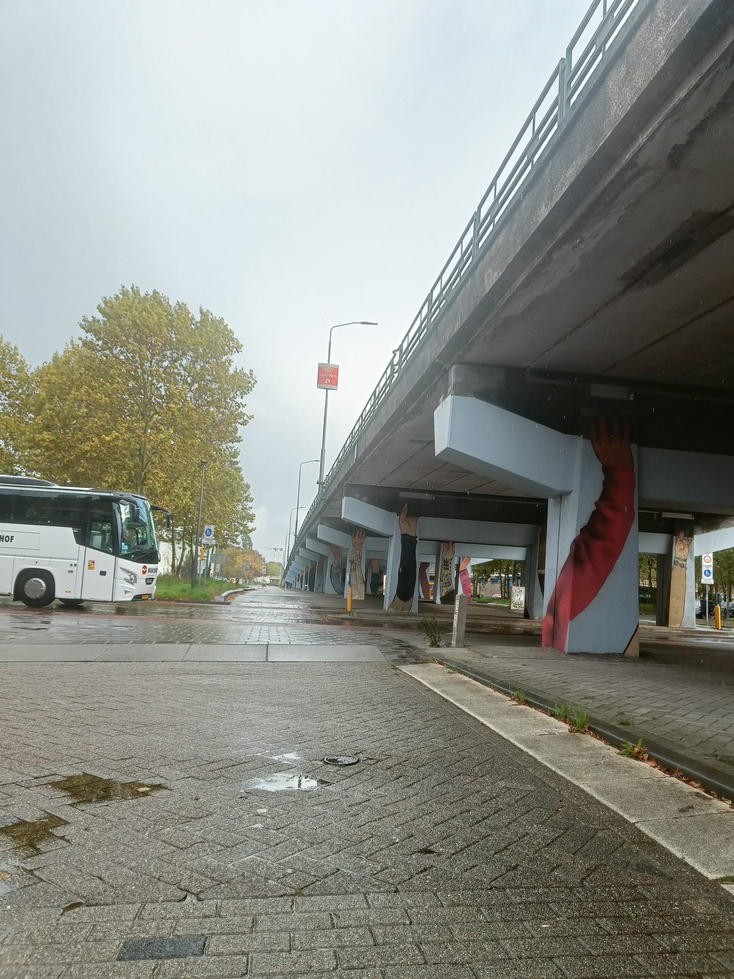 An empty paved space under a concrete viaduct, with a coach parked beyond