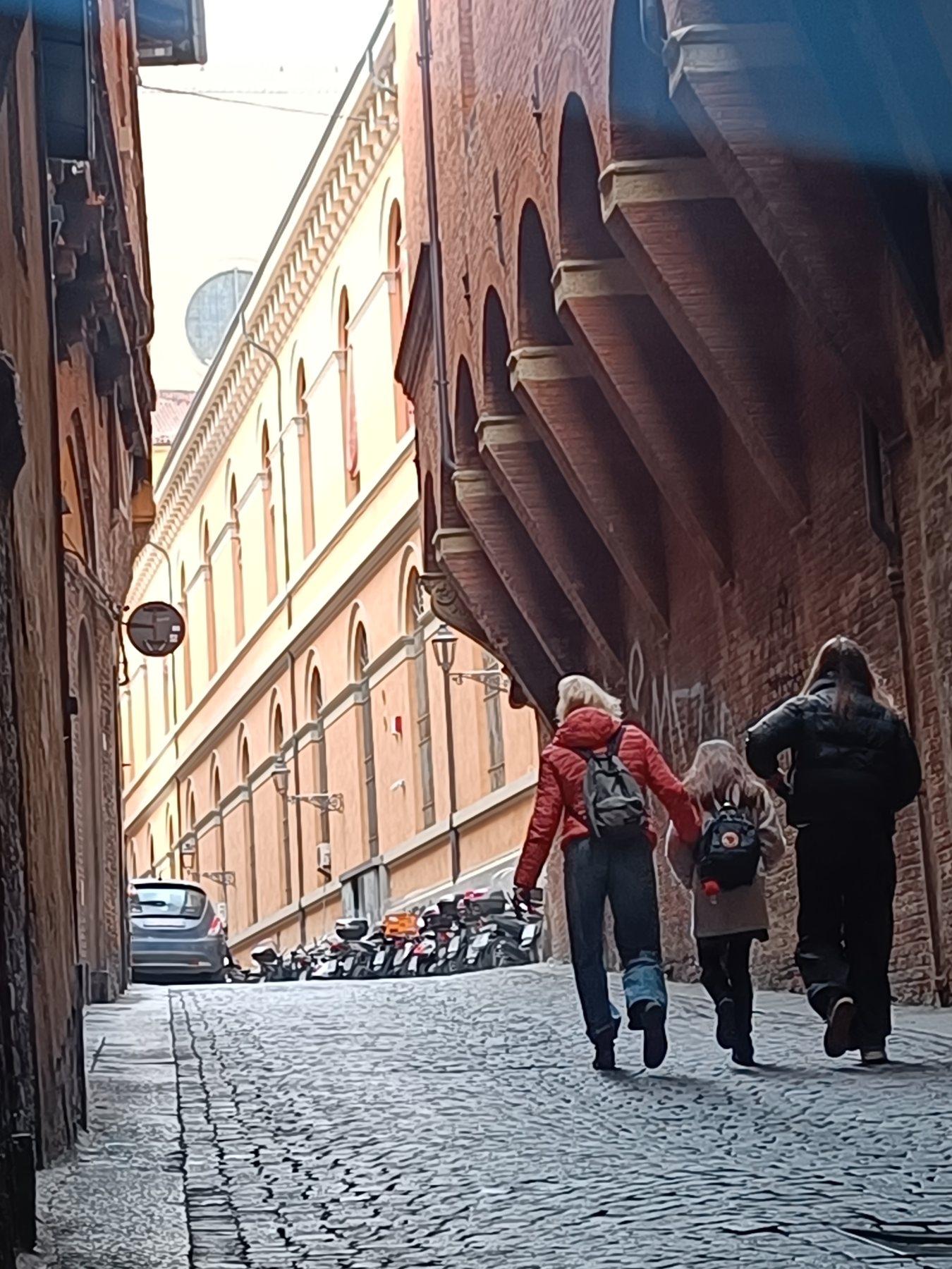 Three people with backpacks walking away down a cobbled street under brick arches