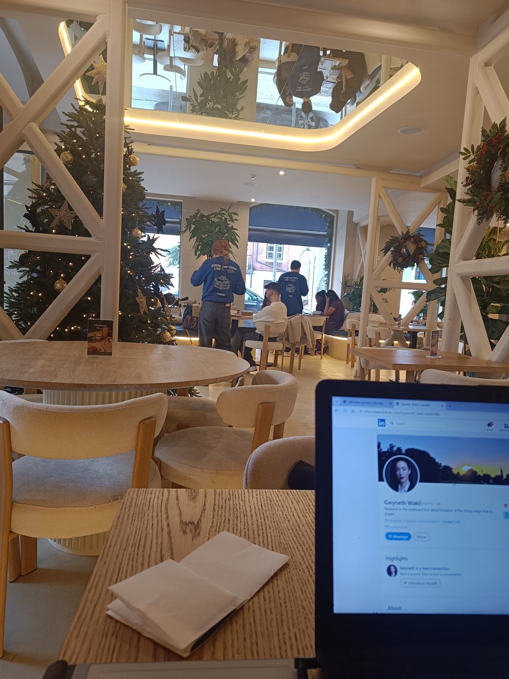 A busy café interior with Christmas decorations and staff at work, a laptop open in the foreground