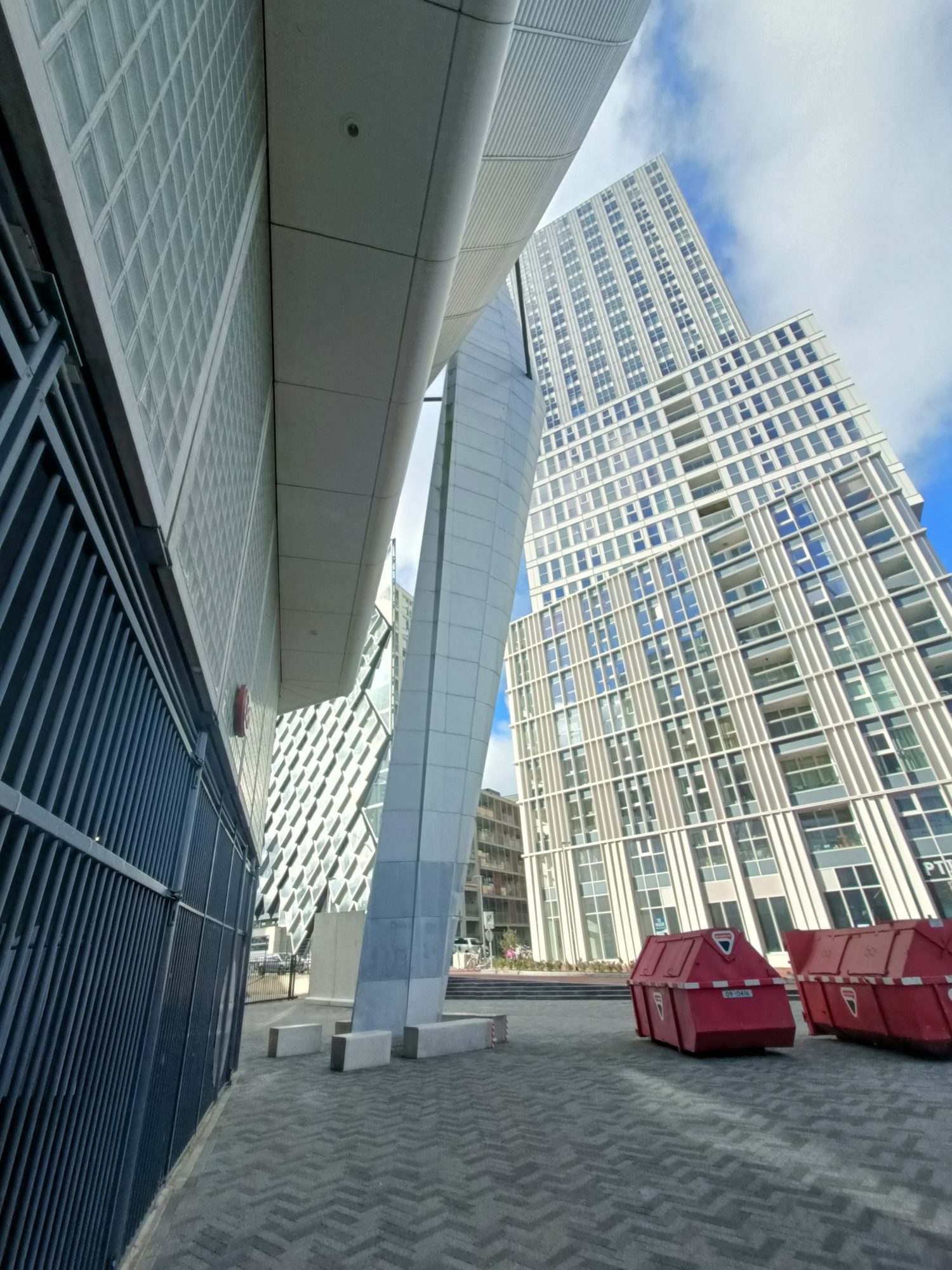 New high-rise towers seen from below, with red waste containers at their foot